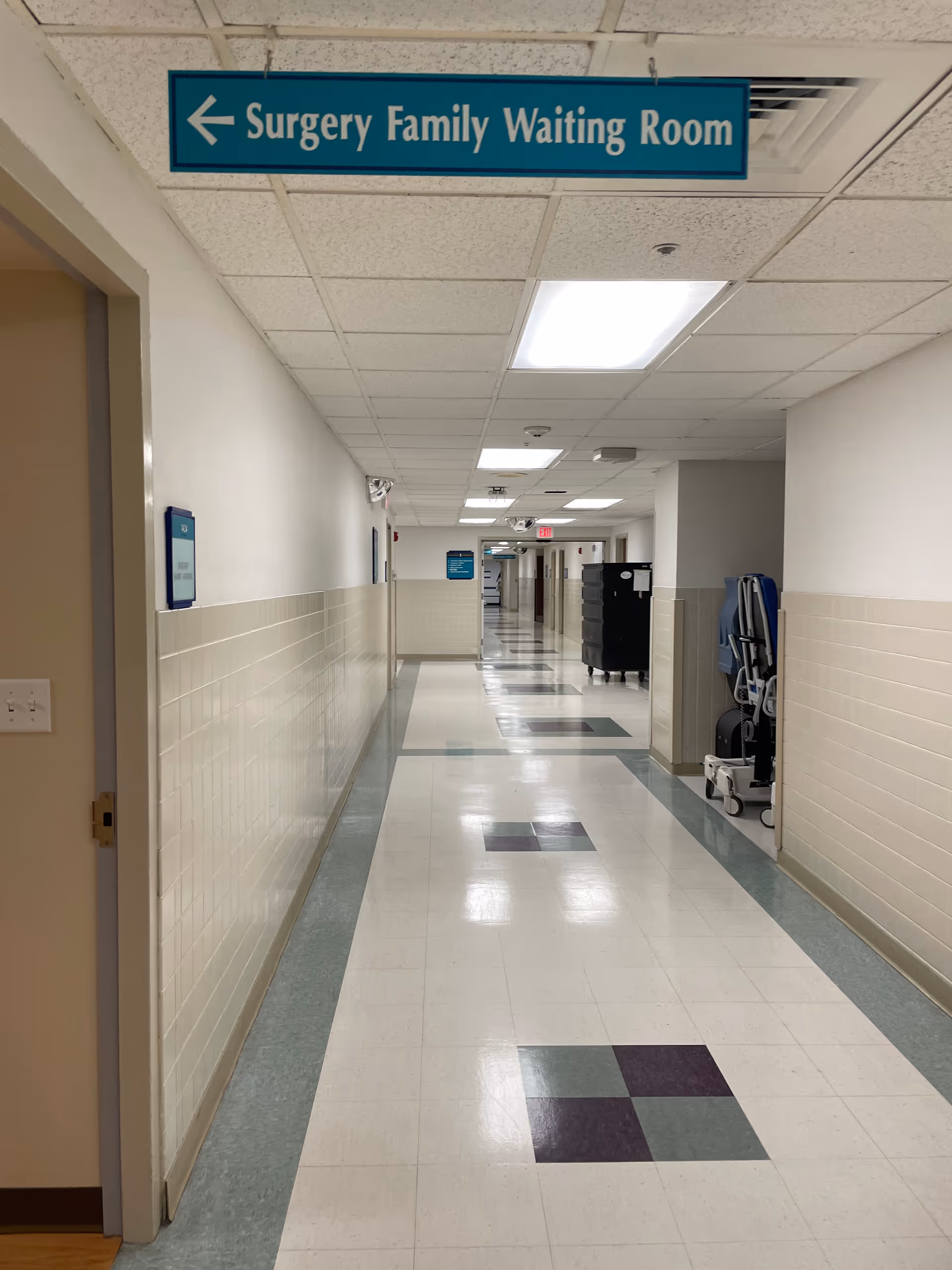 Long hospital corridor with overhead blue Surgery Family Waiting Room sign.