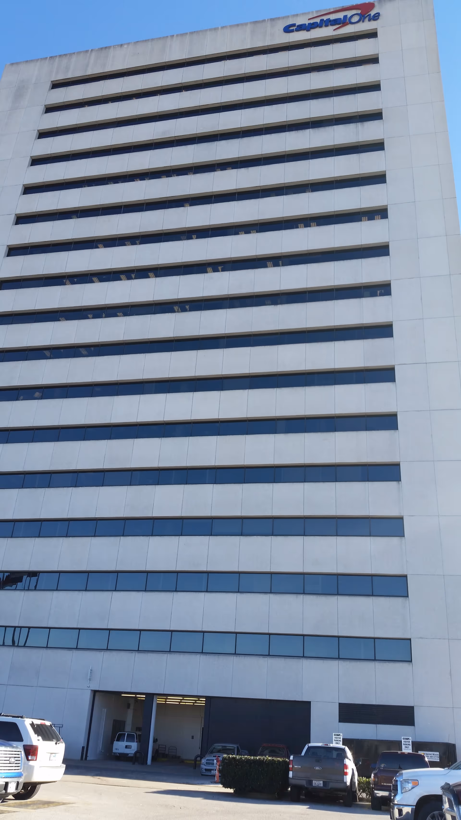 Tall white Capital One office building with many windows and a parking area.