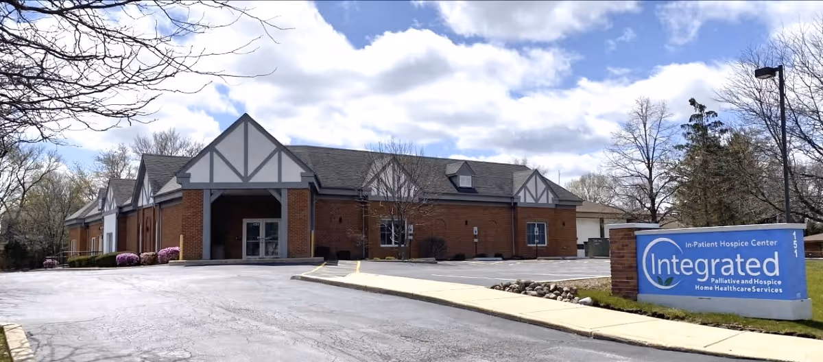 Brick building exterior with a covered entrance and a blue Integrated Palliative and Hospice sign.