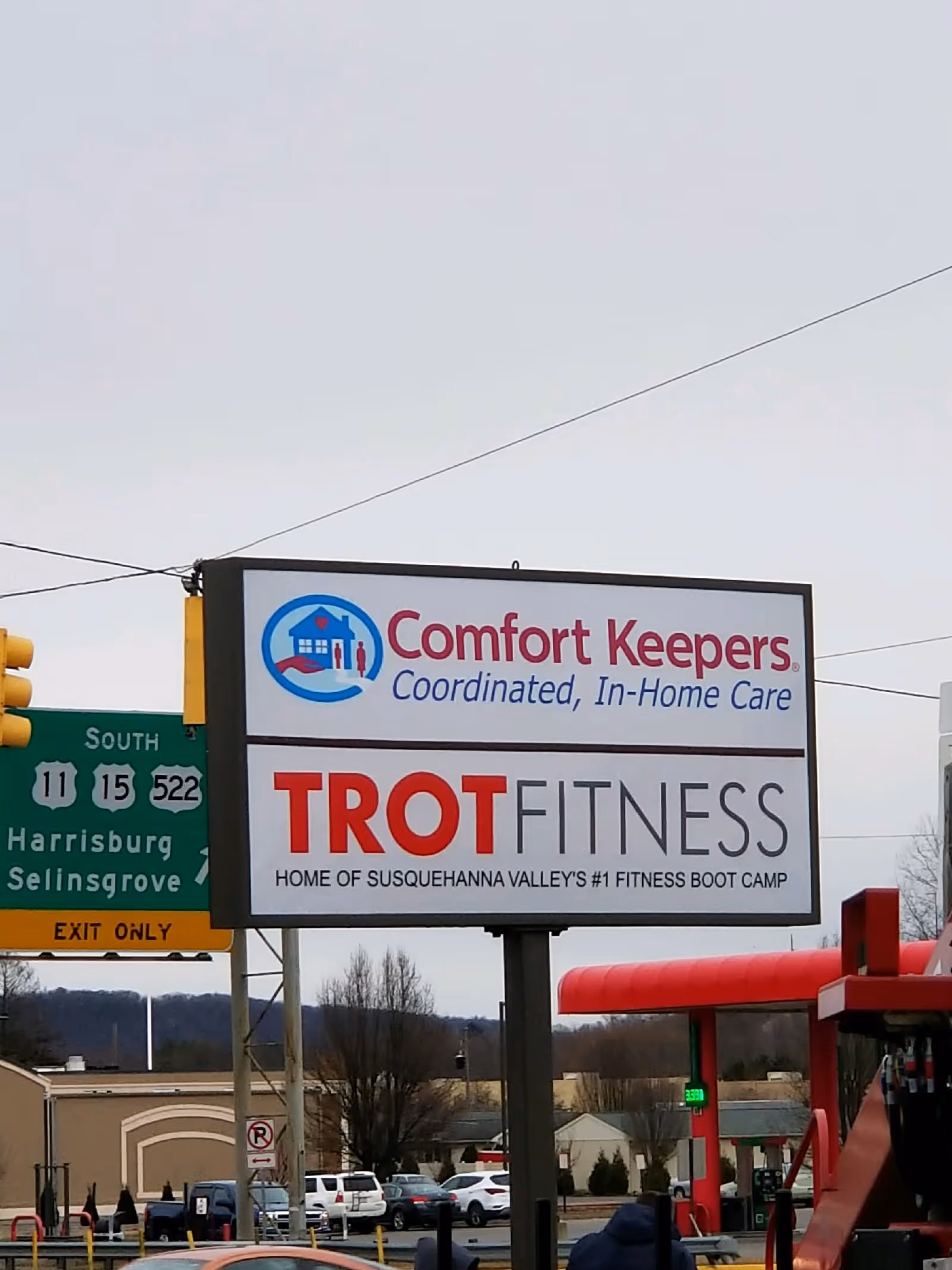 Roadside sign display featuring Comfort Keepers and TROT Fitness beside a roadway.