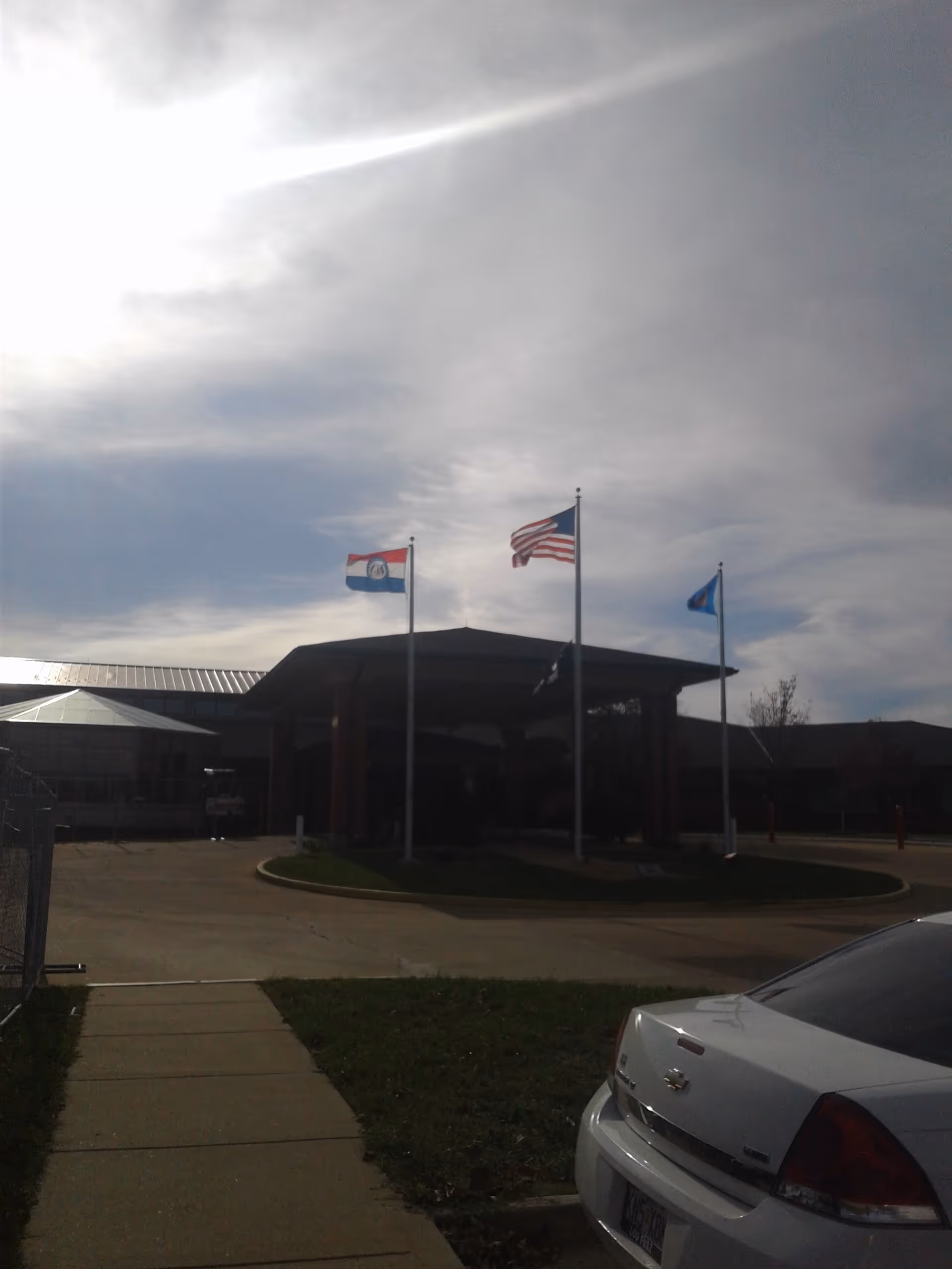 Exterior view of Missouri Veterans Home entrance with flagpoles and a parked car.