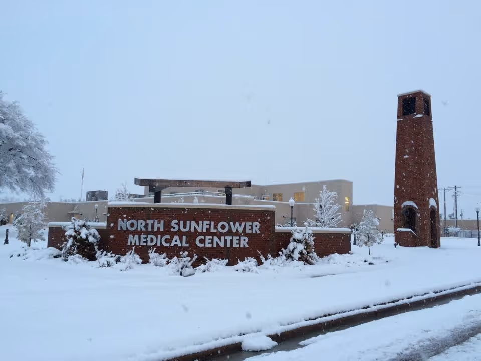 Snow covers brick building front with a tall tower and North Sunflower Medical Center sign.