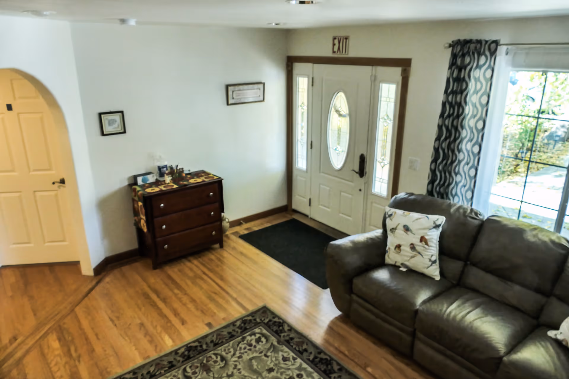 Bright living area by the front door, with sofa, curtains, and a dresser.