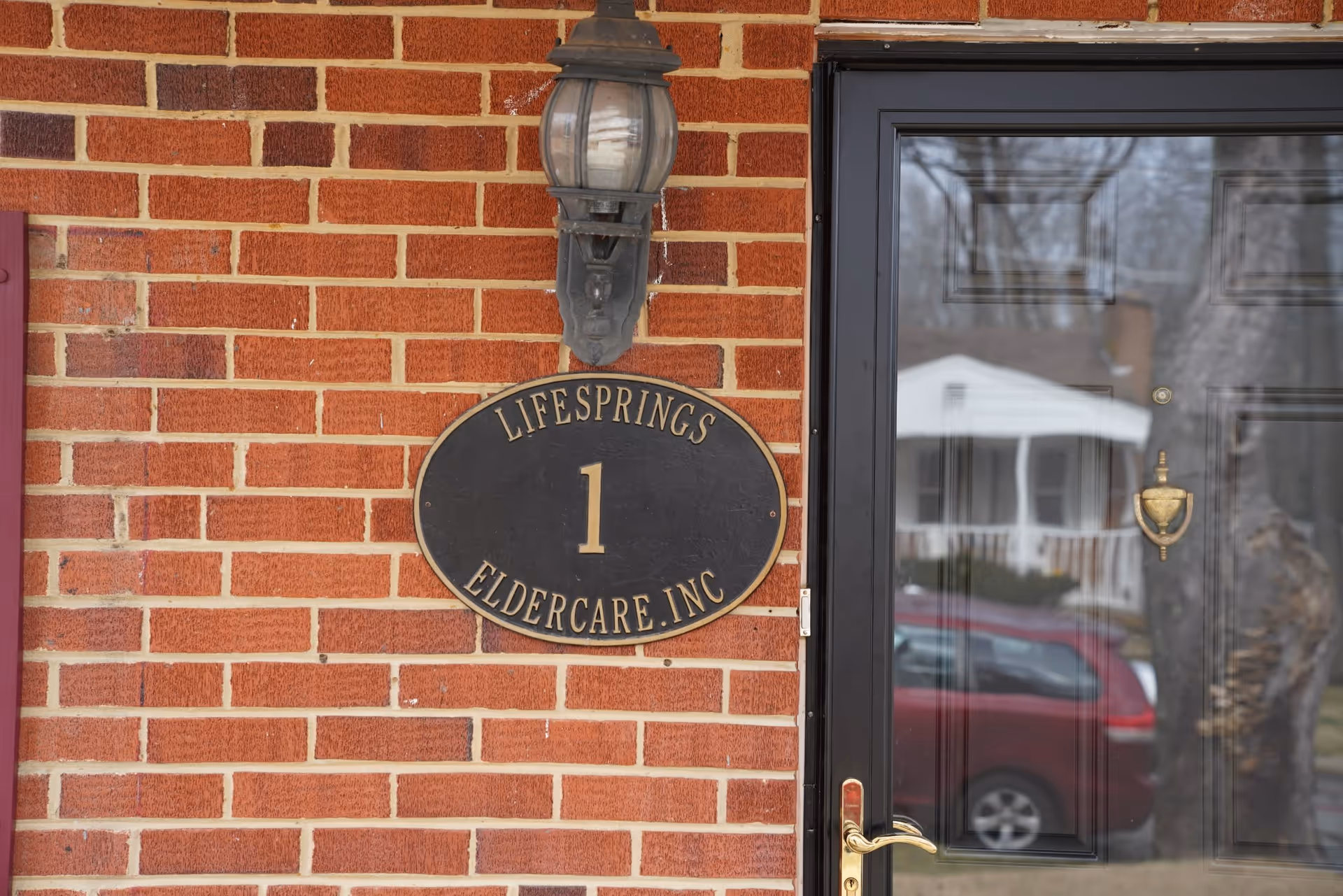 Brick exterior with a black front door and oval Lifesprings Eldercare sign.