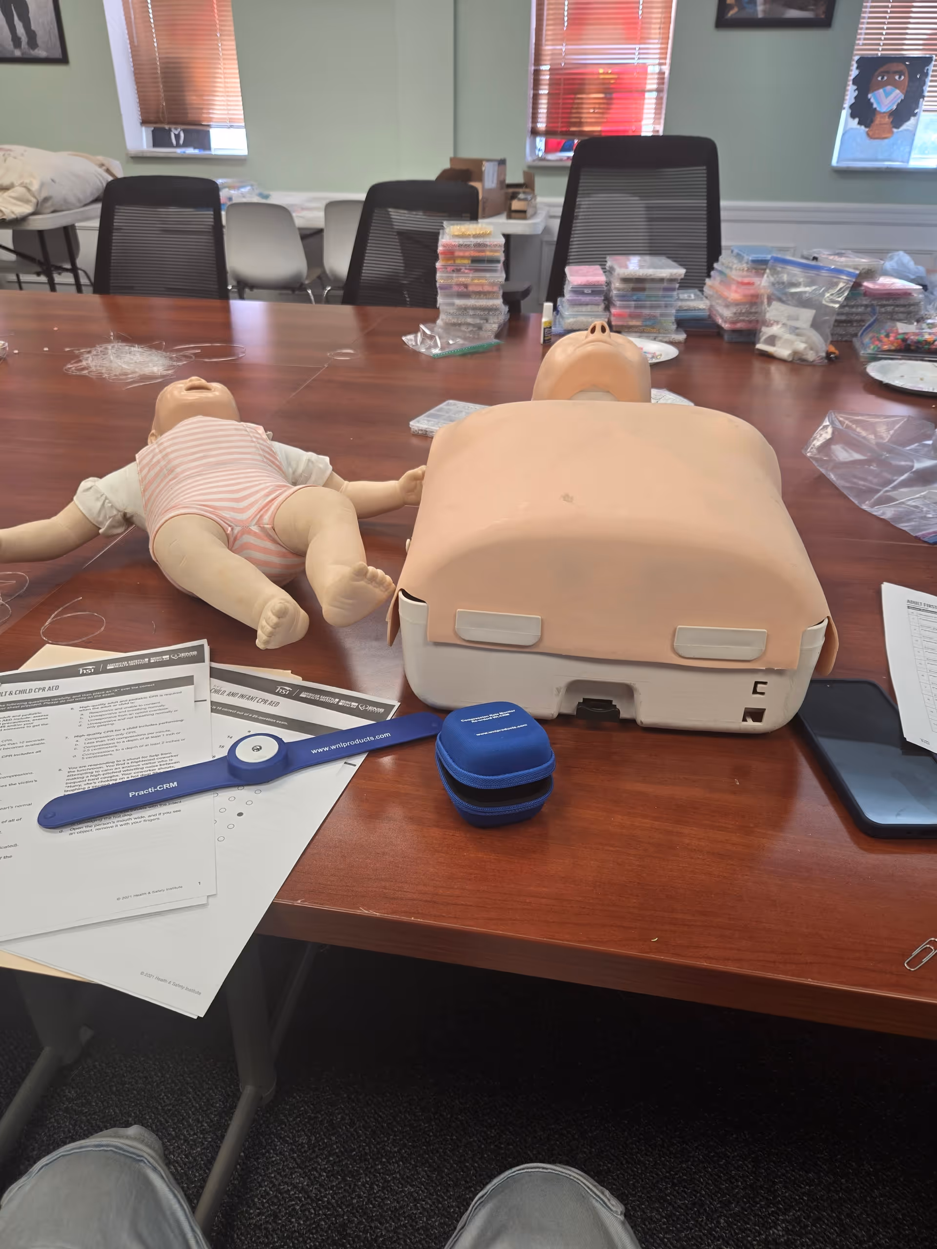 CPR training manikins and supplies on a conference table in a classroom setting.