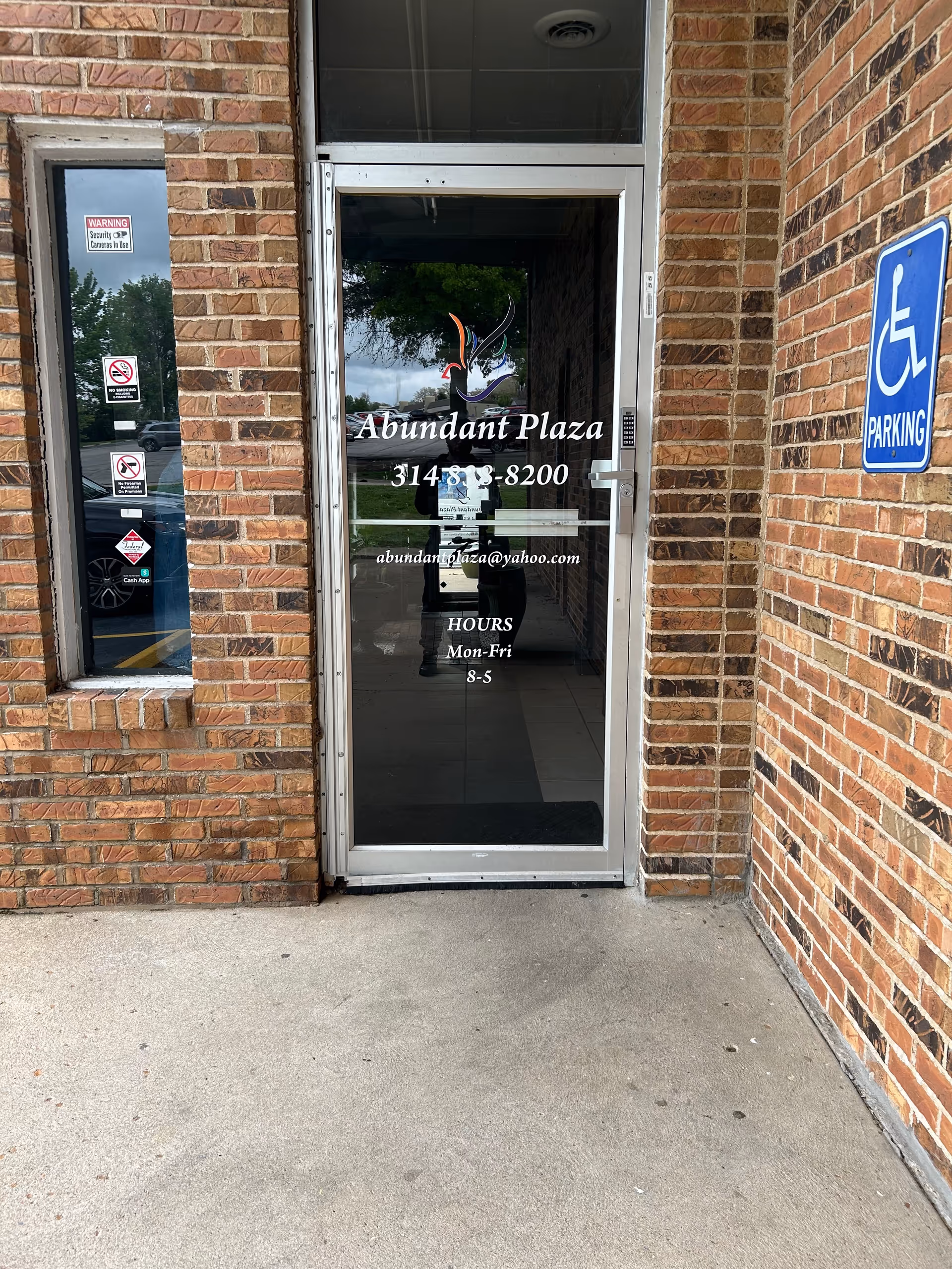 Brick building entrance with glass door displaying Abundant Plaza signage and a handicapped parking sign.