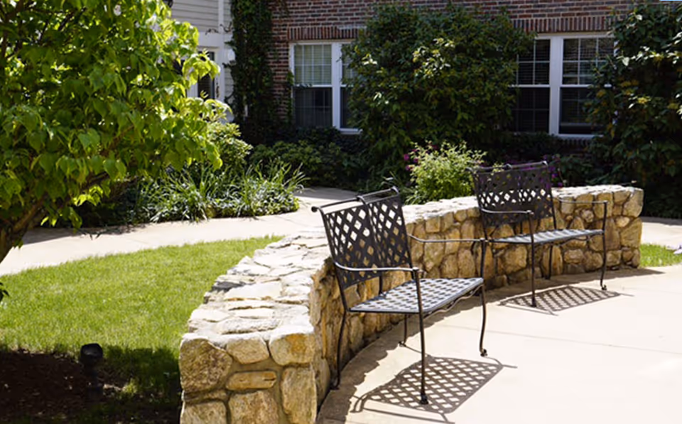 Outdoor courtyard with two metal chairs beside a stone wall.