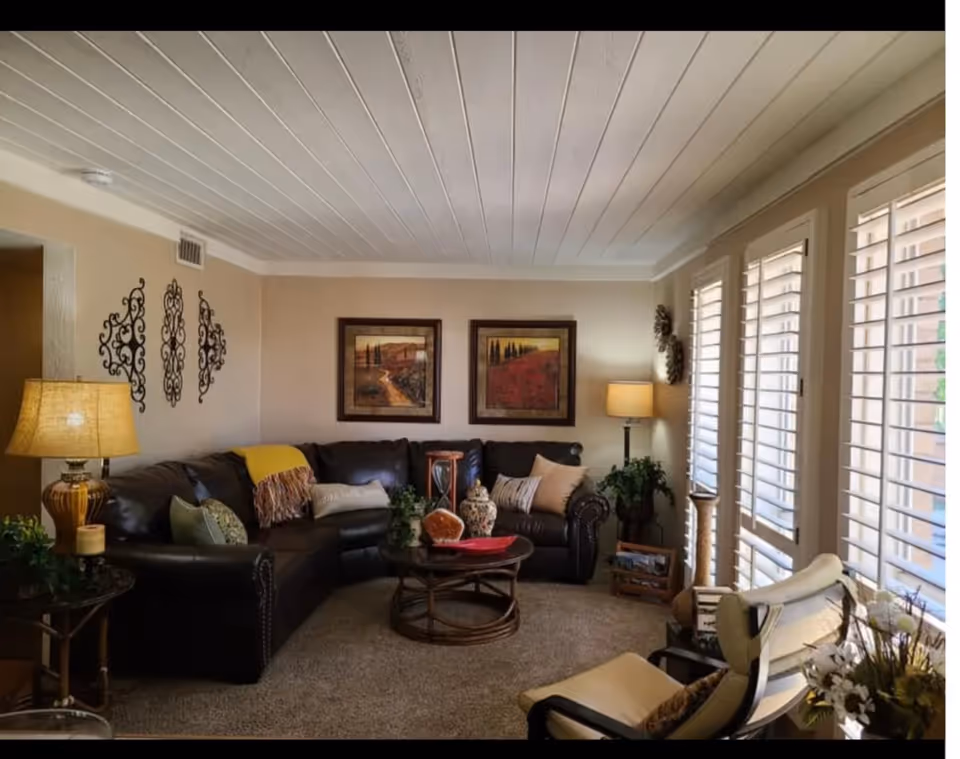 Cozy living room in a senior facility with leather sofa, tables, lamps, and large windows.