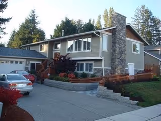 Two-story senior living home exterior with stone chimney, driveway, and landscaped yard.