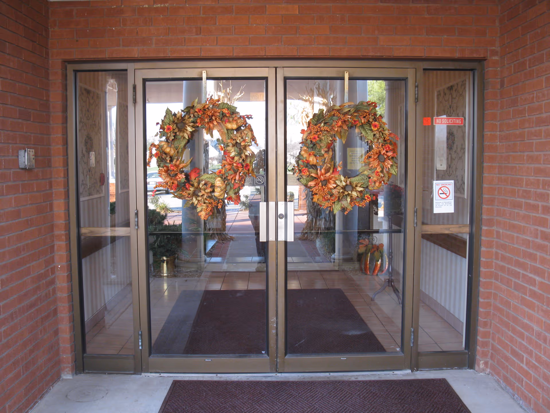 Red brick facility entrance with glass doors and two autumn wreaths.