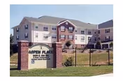Exterior view of Aspen Place senior living building with a brick sign and fence.