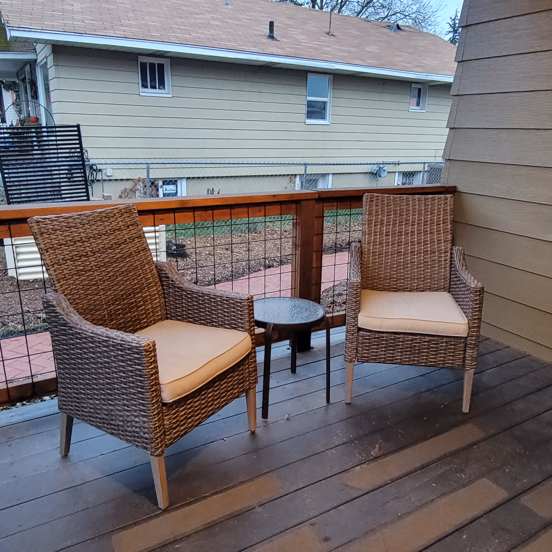 Two cushioned wicker chairs surround a small table on an outdoor wooden balcony.