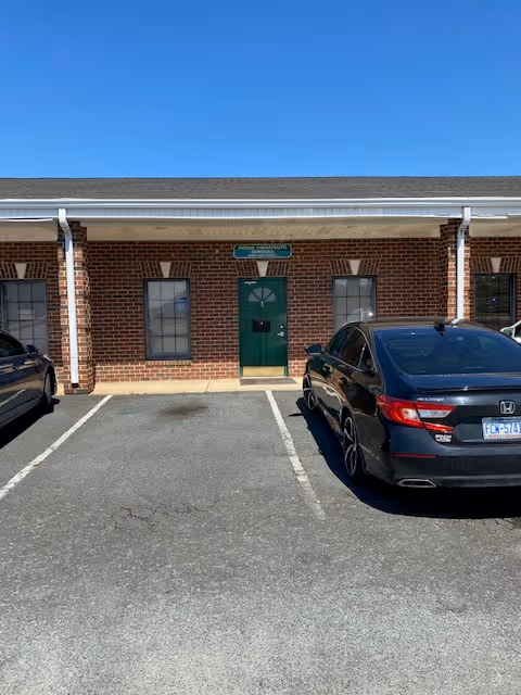 Brick facility exterior with a green front door and parked cars in a lot.
