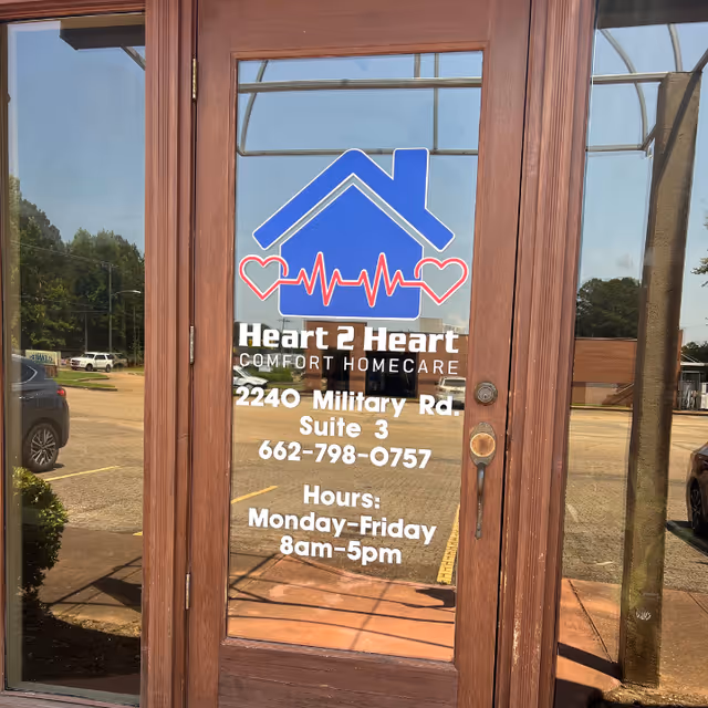 Wood-framed glass door displays Heart 2 Heart Comfort Homecare logo, address, and hours