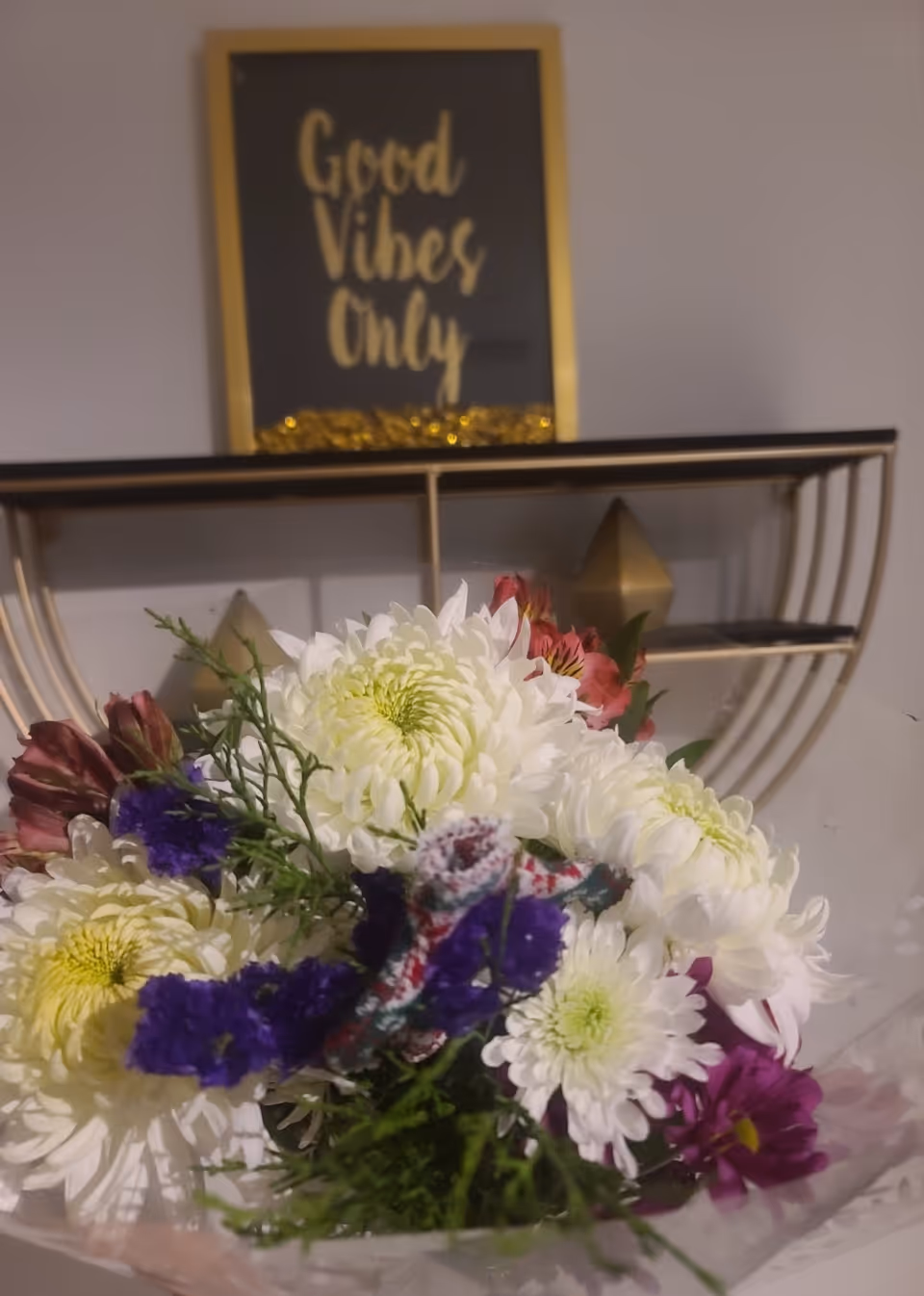 Bouquet of white flowers with colorful accents sits in front of a Good Vibes Only sign.