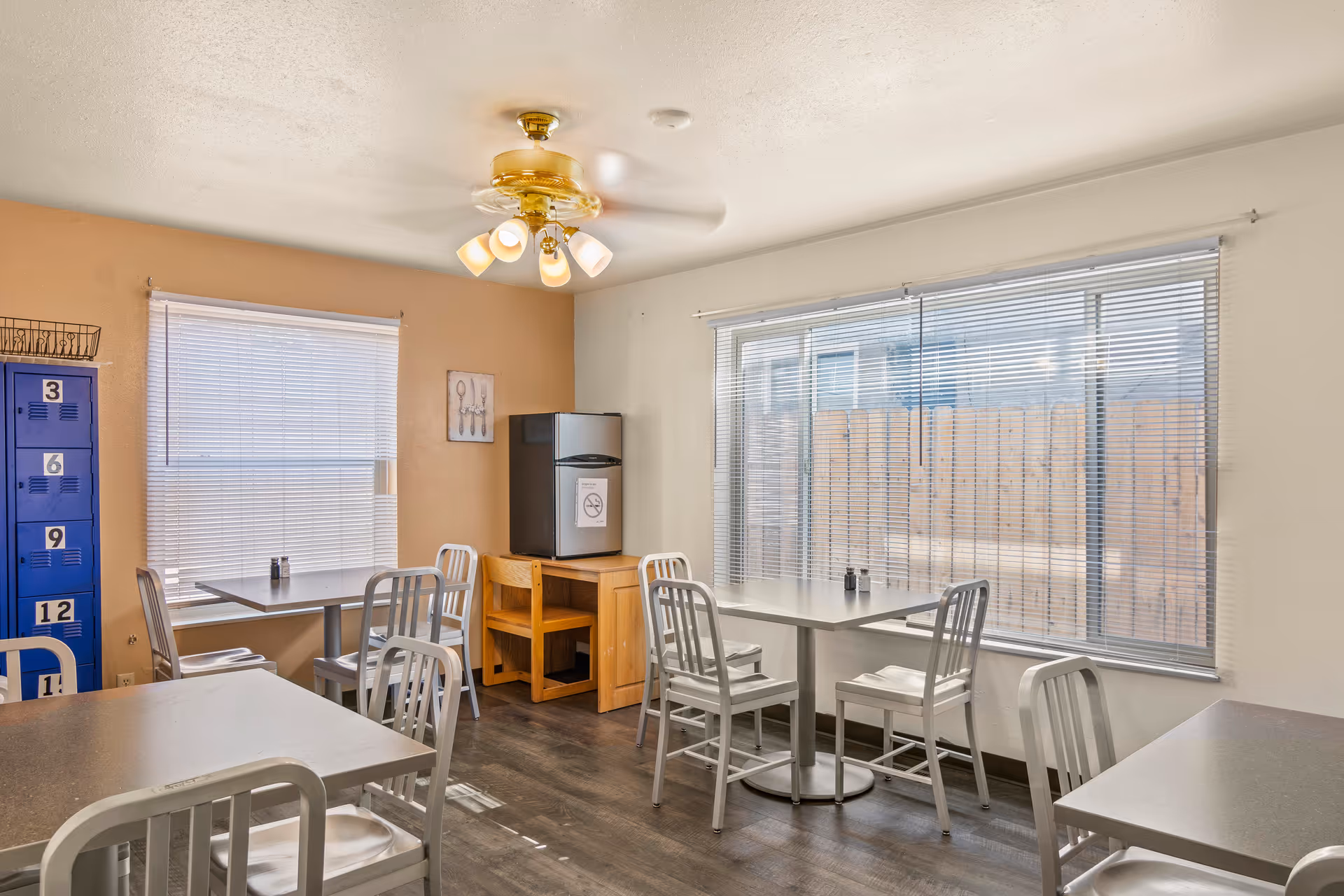 Bright dining area with metal chairs, tables, a water cooler, and large windows.