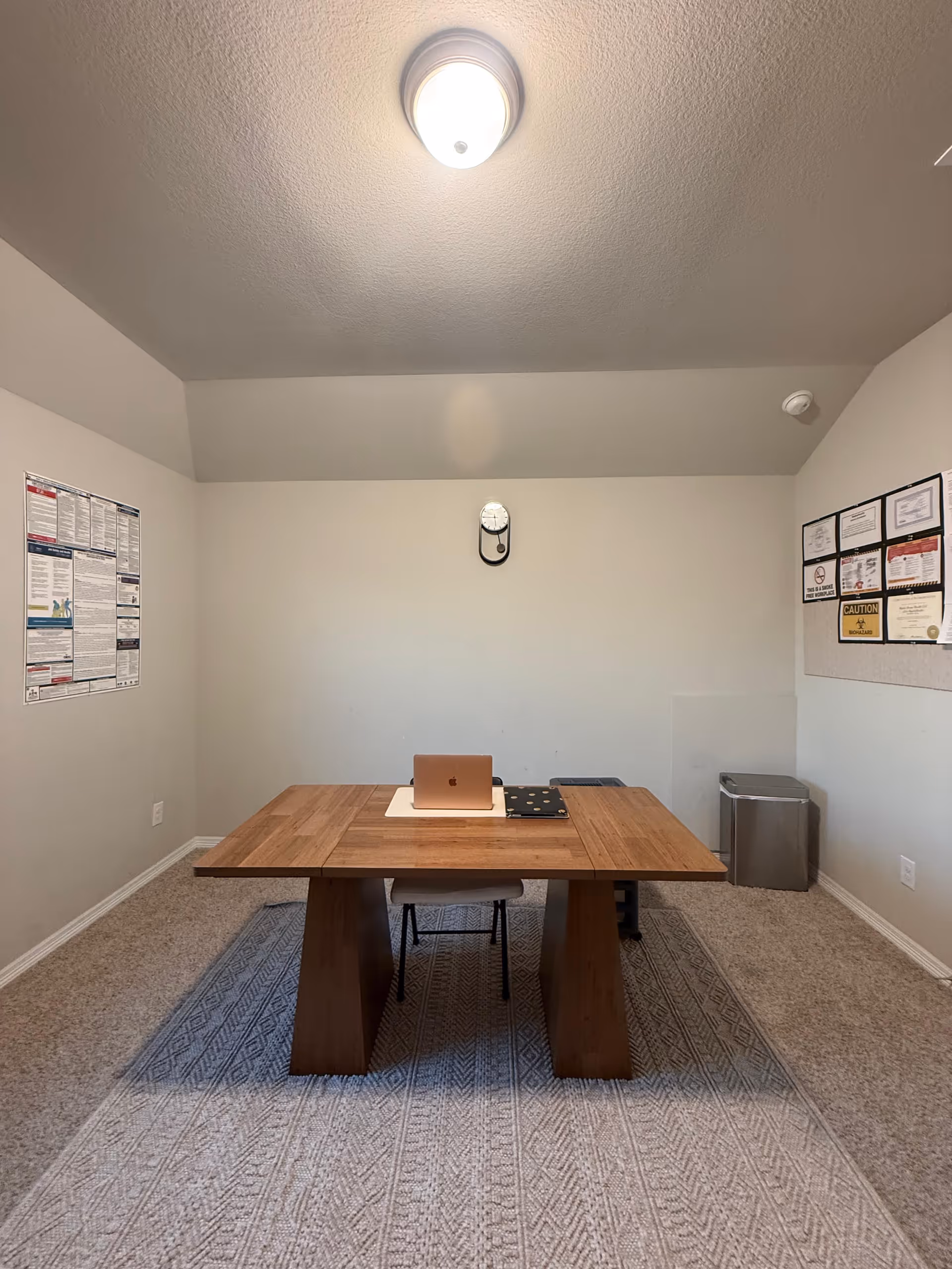 A wooden table with laptop and chair in a small, plain meeting room.