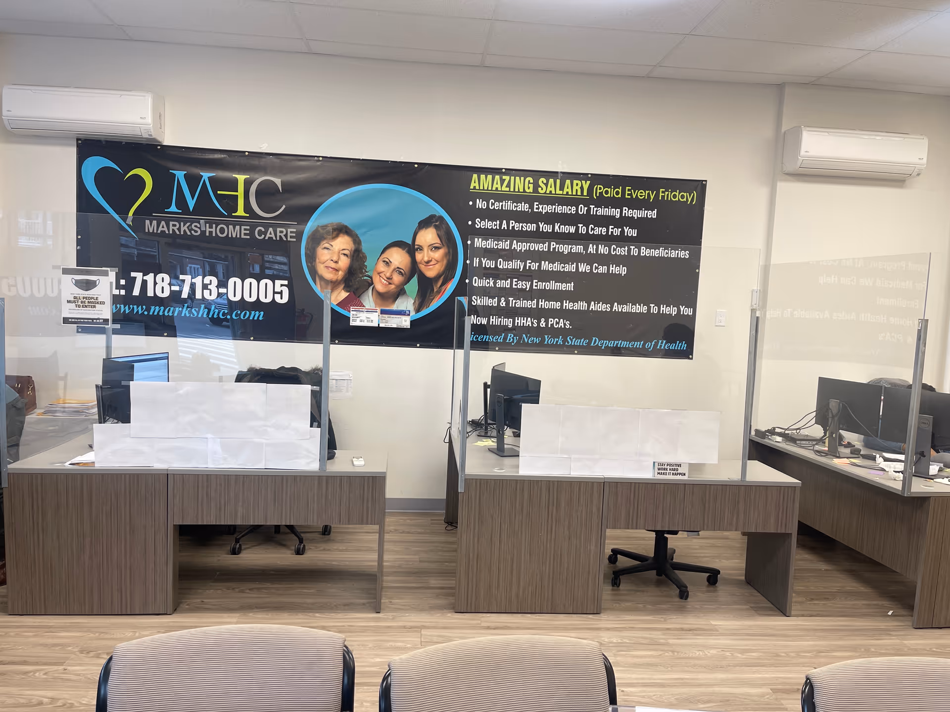 Office reception area with desks, glass dividers, and a large Marks Home Care banner.