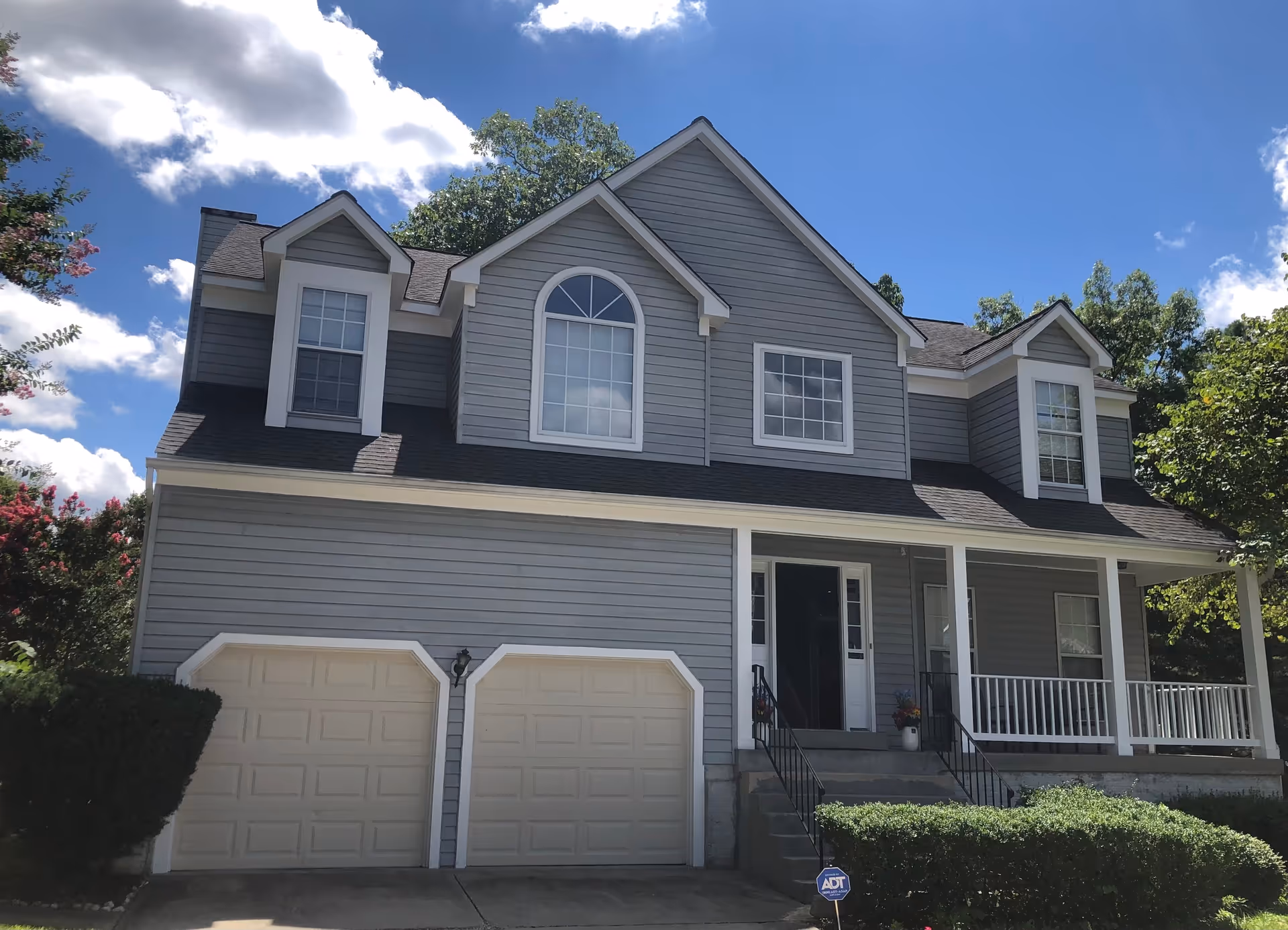 Front exterior of a two-story gray house with a two-car garage and covered porch under a blue sky.