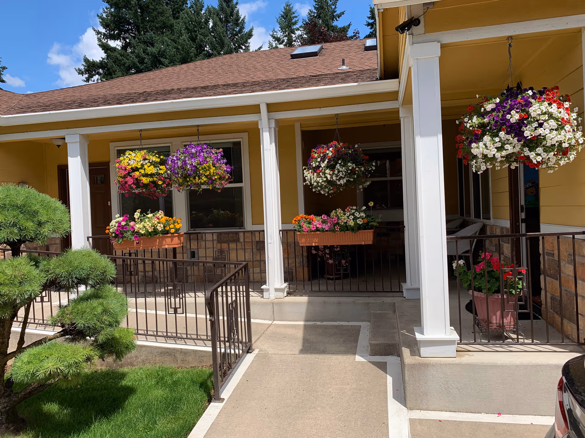 Exterior of a yellow senior living facility with hanging flower baskets.