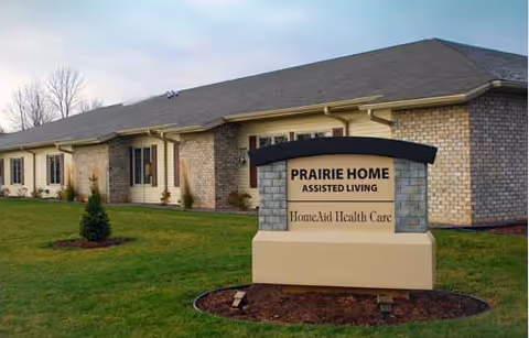 Exterior view of Prairie Home Assisted Living facility with a front sign on lawn.