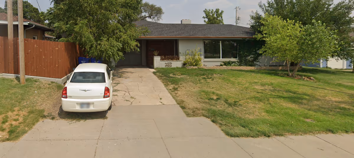 Front view of a single-story home with driveway, yard, and a white car.