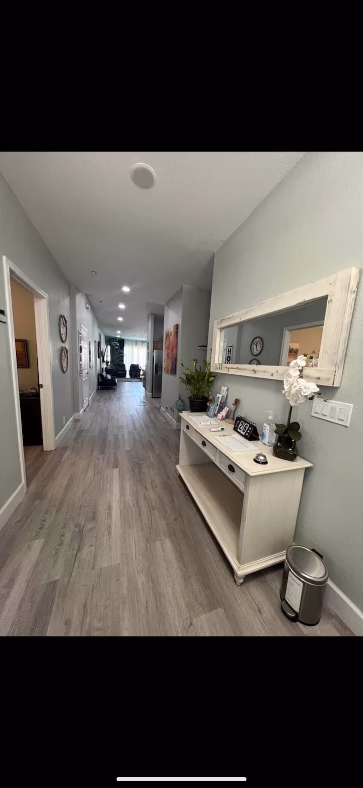 Bright hallway inside a senior living facility featuring a console table, large mirror, and decorative plants.