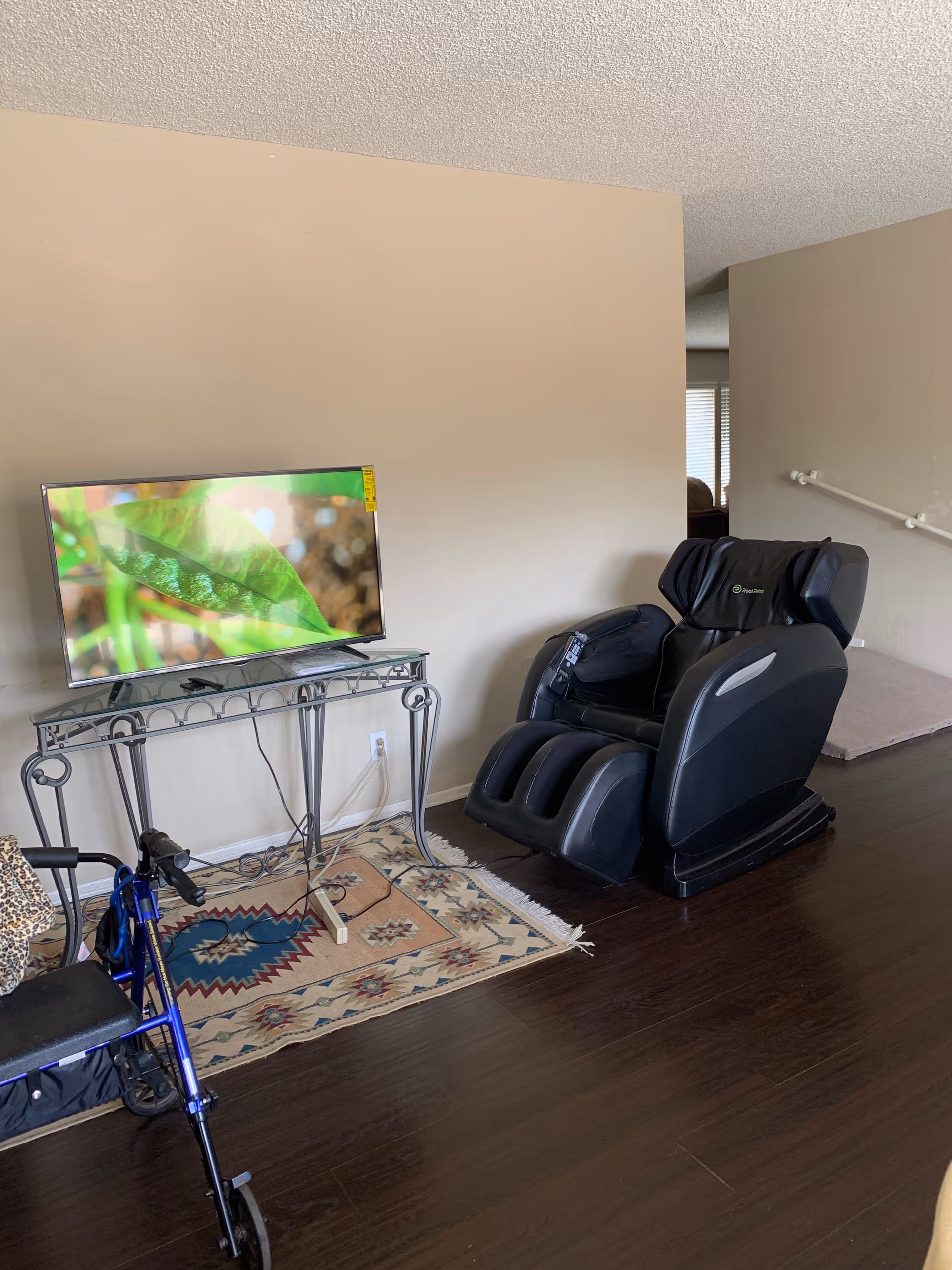 Television on a glass console faces a black massage chair in a cozy living area.