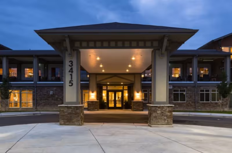 Exterior view of a senior living facility entrance with a covered driveway and warm lights.