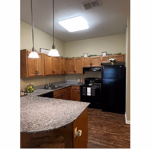 Cozy kitchen with wooden cabinets, granite counters, pendant lights, and black appliances.