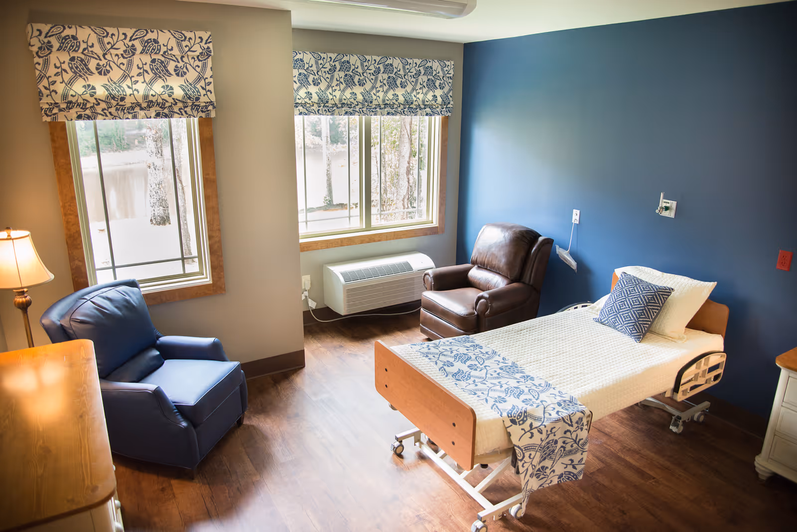 A tidy patient room with a bed, chair, and large windows.