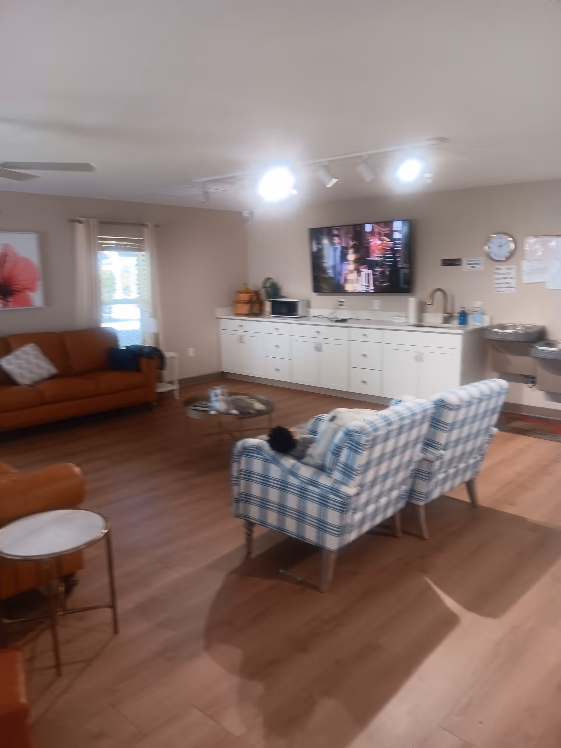Cozy living room in a senior facility with a TV, cabinets, and plaid chairs.