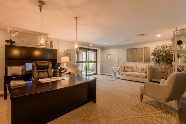 Reception lobby with a large dark desk and office chair, seating area with sofas and chairs, and glass entrance doors.