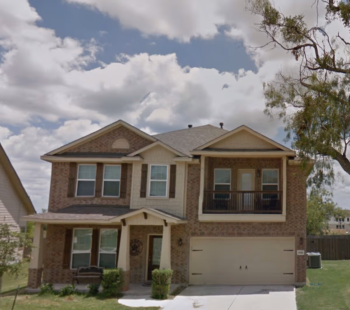 Two-story brick house exterior with front porch, balcony, and two-car garage.
