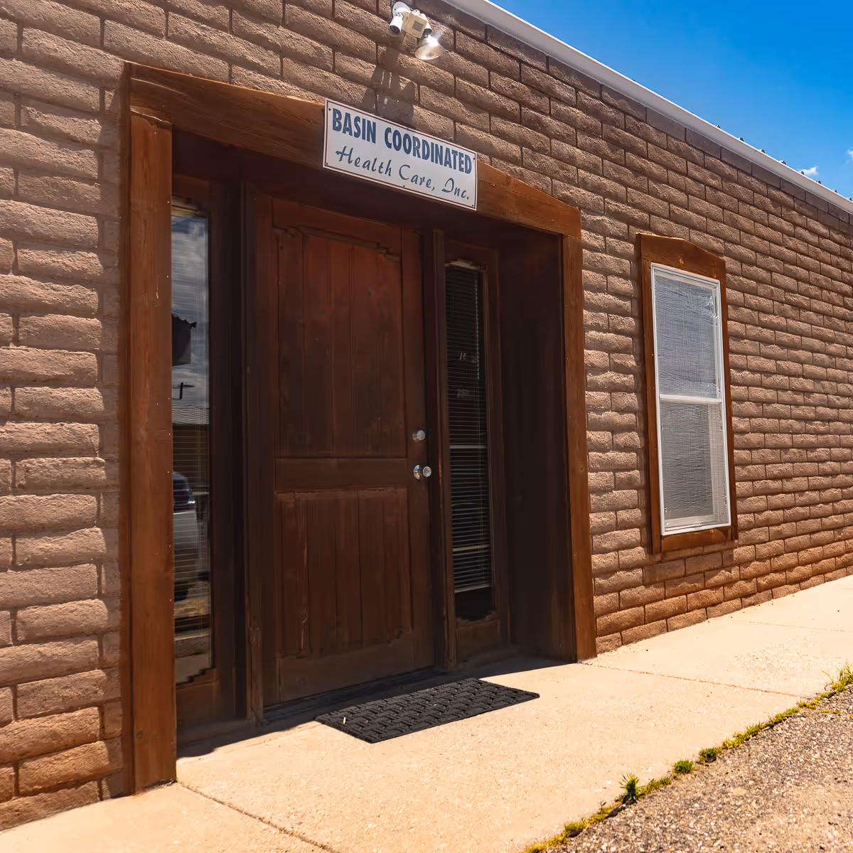Brick building facade with wooden front door and Basin Coordinated Health Care sign.