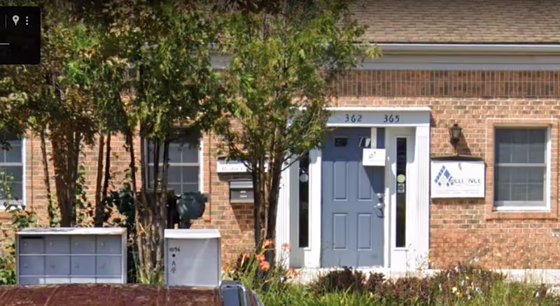 Brick building entrance with blue door, trees, and Alliance Care signage.