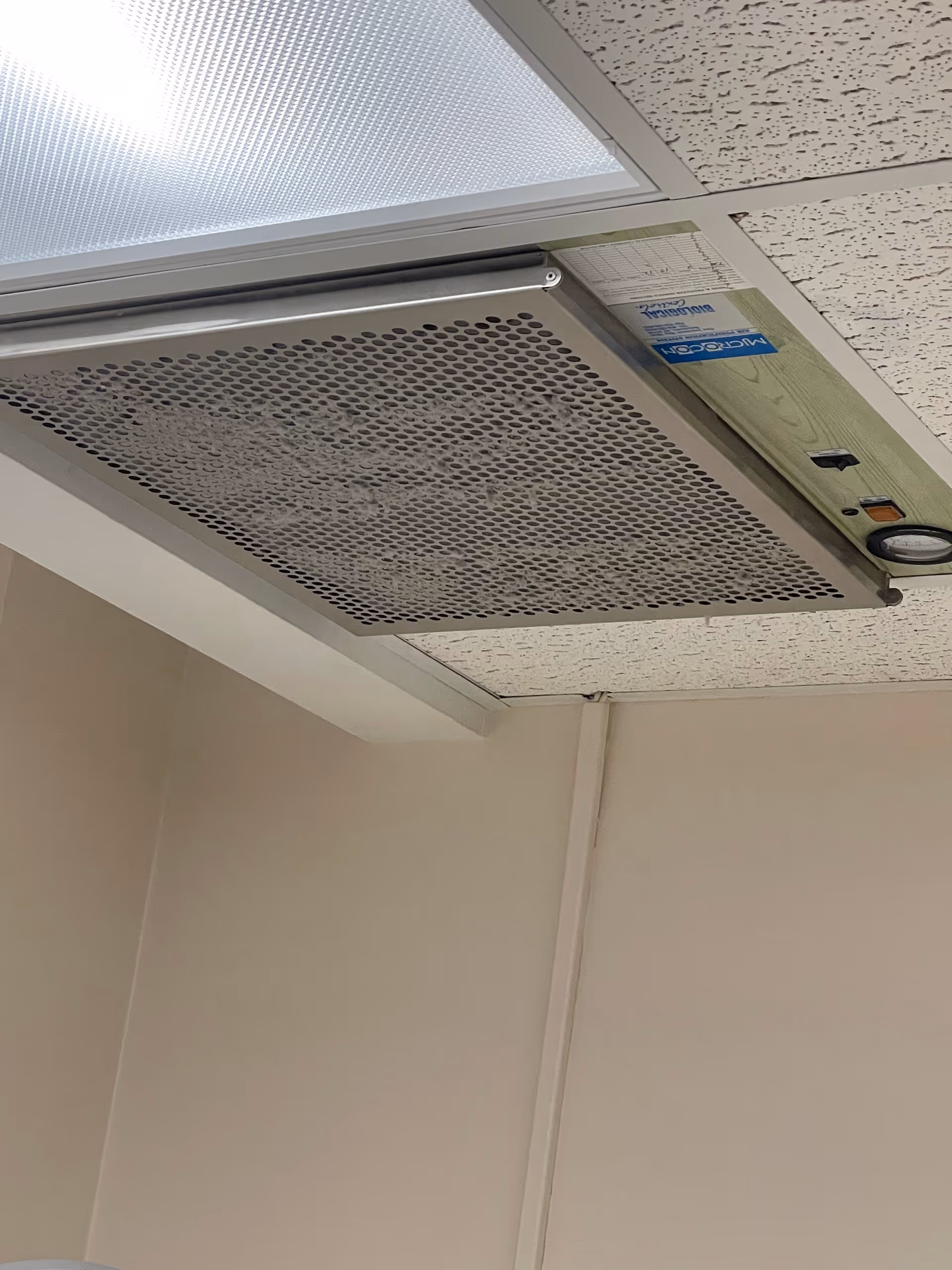 Close-up view of a ceiling-mounted ventilation unit in a beige interior room.
