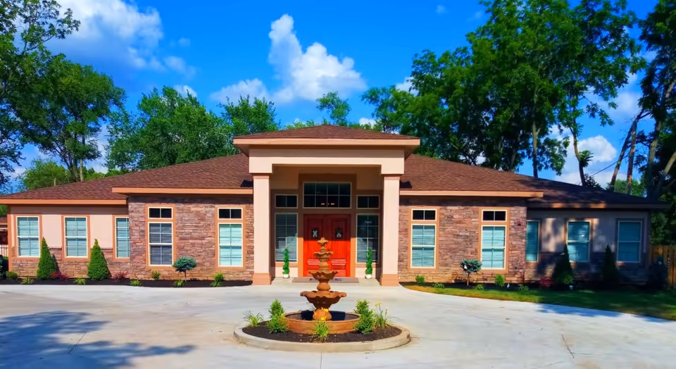 Single-story brick senior living facility with central entrance, fountain, and surrounding trees.