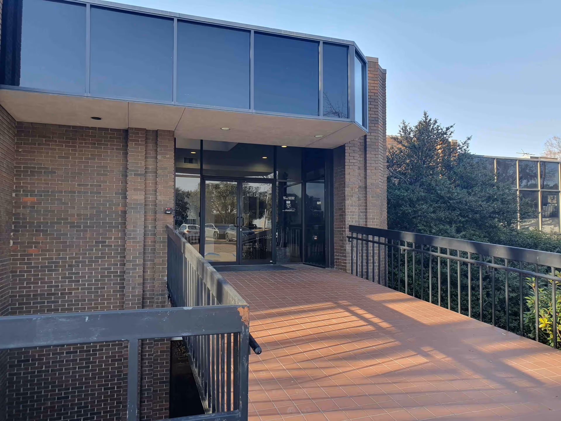 Exterior view of a brick building entrance with glass doors and a tiled ramp