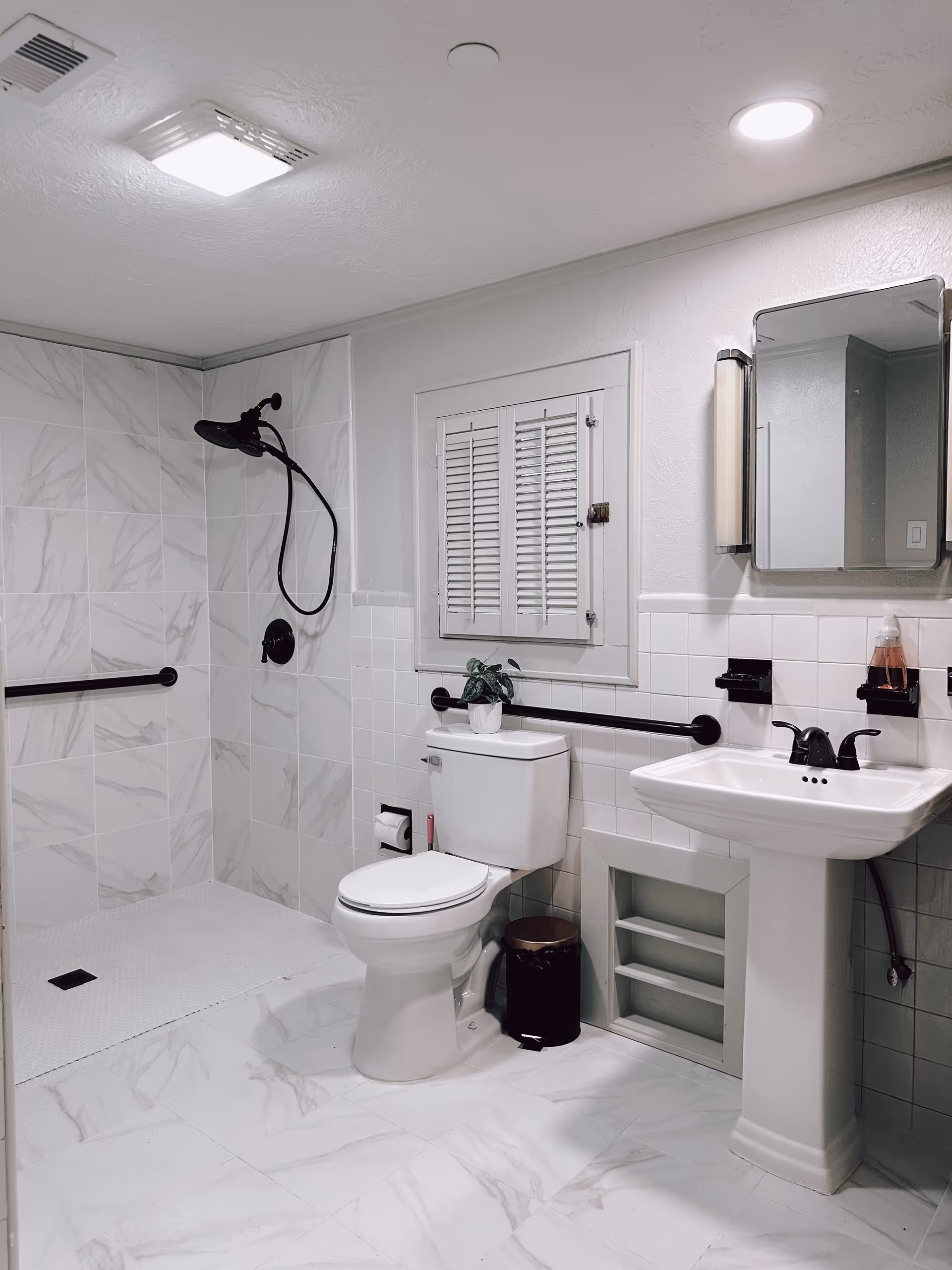 Clean tiled bathroom with shower, handheld showerhead, toilet, sink, and grab bars.