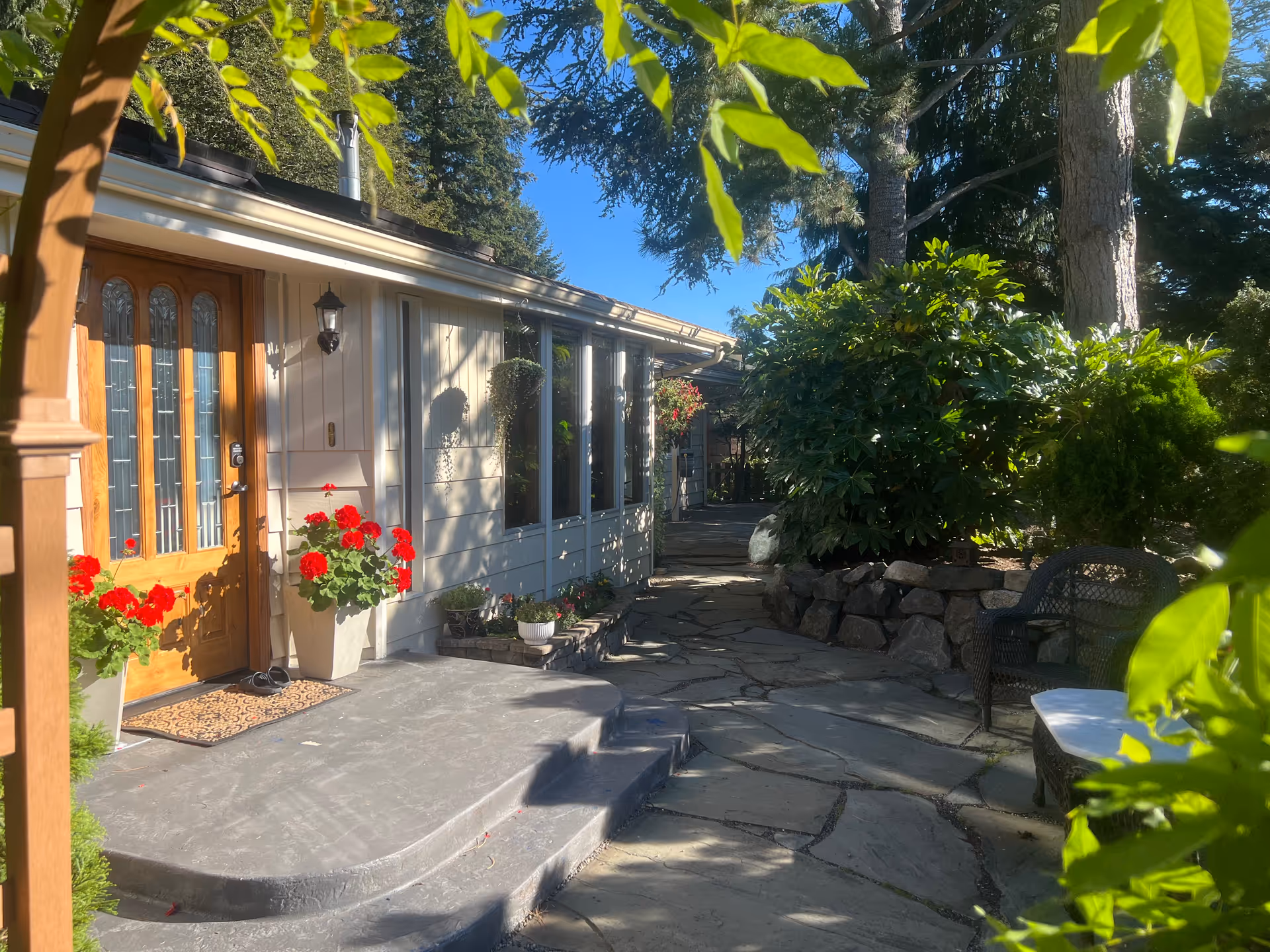 Exterior of Bahji Gardens Adult Family Home with front door, red flowers, and outdoor seating.
