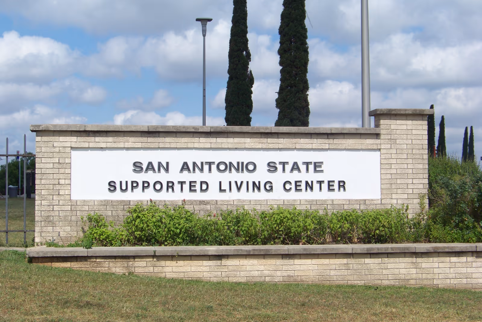 Brick sign reads 'San Antonio State Supported Living Center' with shrubs.