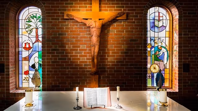 An altar with a crucifix flanked by stained glass windows inside a chapel.