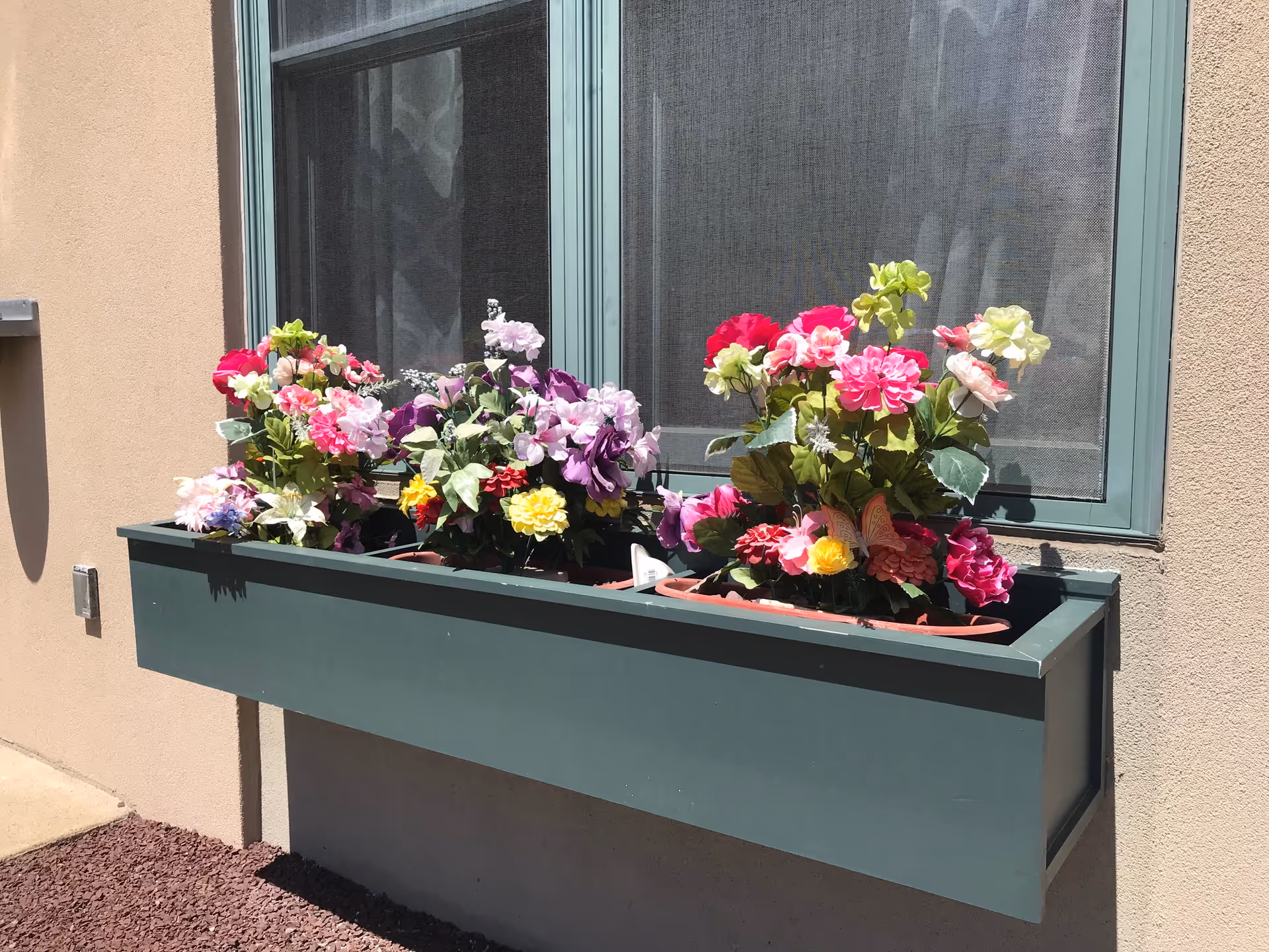 Rectangular outdoor planter filled with colorful flowers beneath a window.