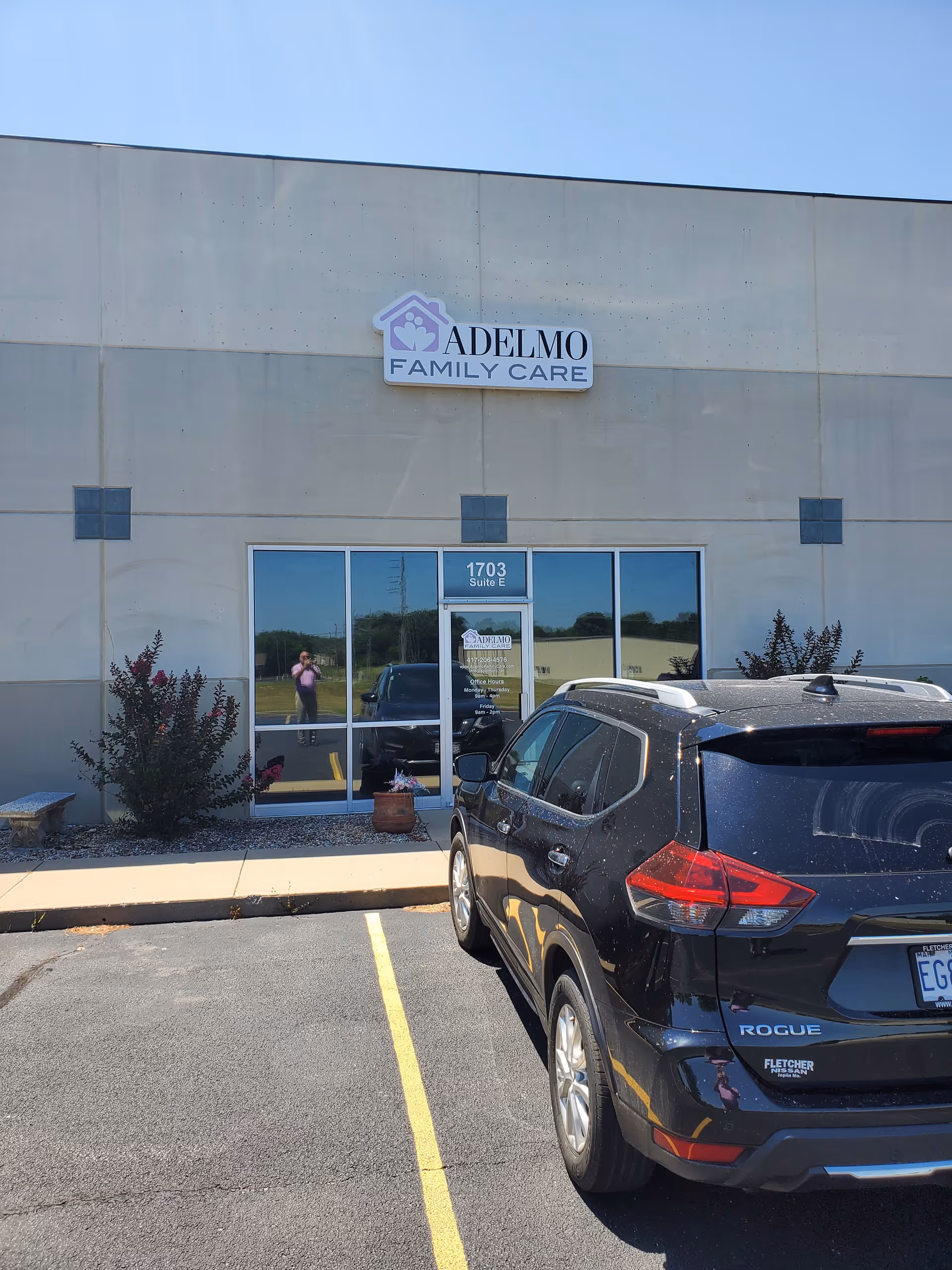 Front view of Adelmo Family Care facility with glass doors and a parked black SUV.