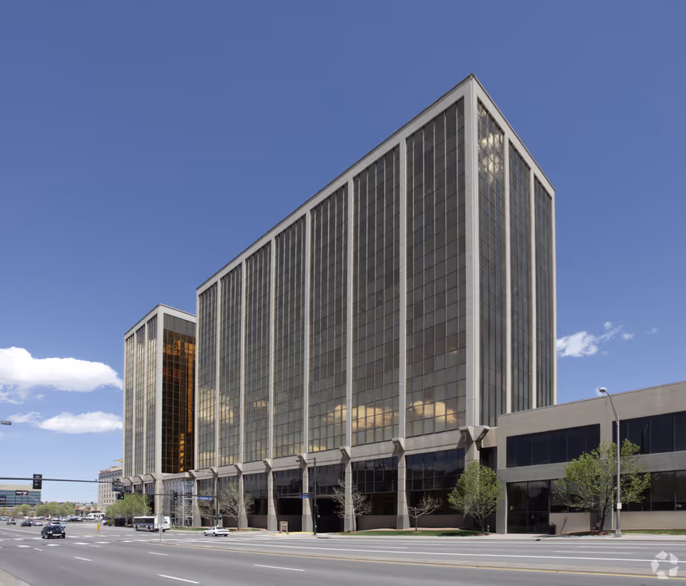 Tall glass-front office building along a street against a clear blue sky.