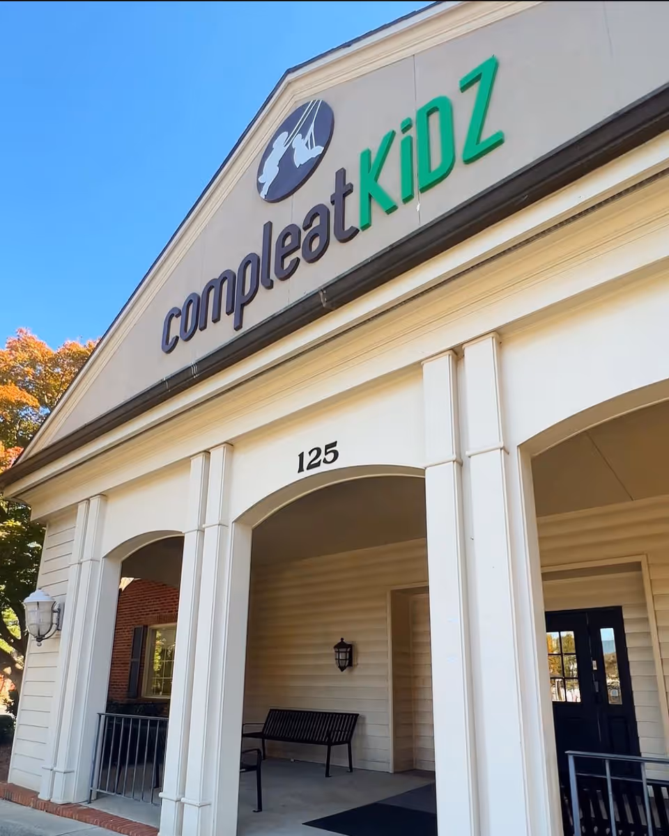 Exterior view of a building front with a green Compleat KiDZ sign and arches.