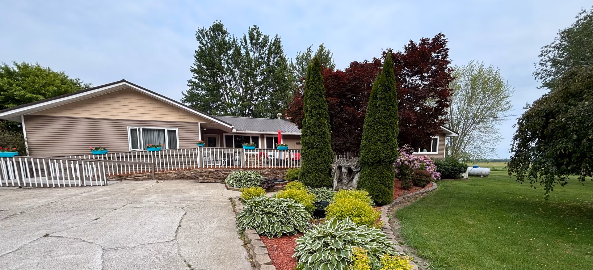 Single-story senior living facility exterior with a white railing, ramp, and landscaped front yard.