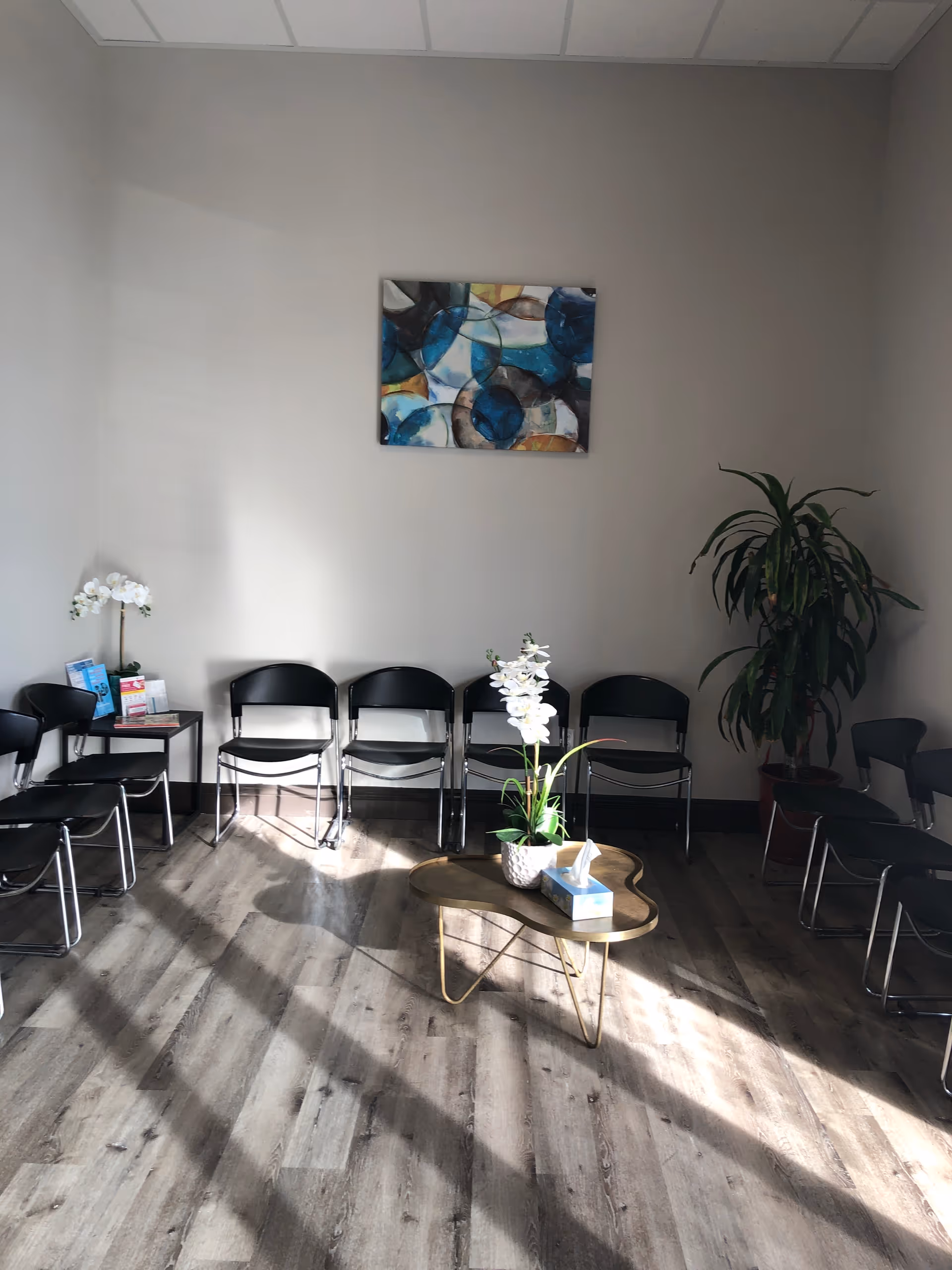 Waiting area with black chairs, a central wooden coffee table, orchids, and wall art.