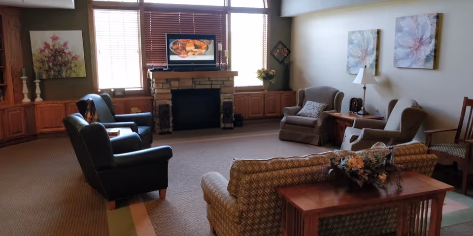 Common living room in a senior facility with sofas, chairs, and a fireplace.